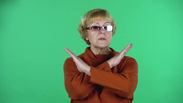 Portrait of senior woman is strictly gesturing with hands crossed making X shape meaning denial saying NO isolated over green background. — Stock Video