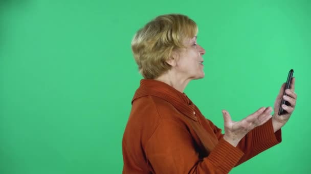 Mujer mayor está hablando para el chat de vídeo utilizando el teléfono móvilaislado sobre fondo verde. Perfil — Vídeos de Stock