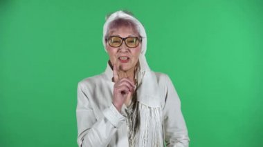 Yaşlı bir kadının portresi fısıldıyor sırrı ve gizli bir jest yapıyor yeşil arka planda izole edilmiş..