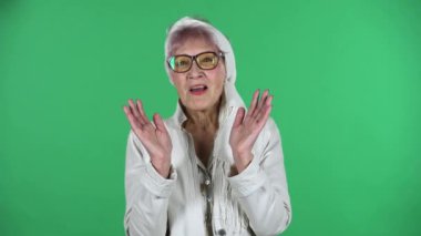 Yaşlı, şık bir kadının portresi, yeşil arka planda saklanmış bir şekilde dümdüz ve gülümsüyor..