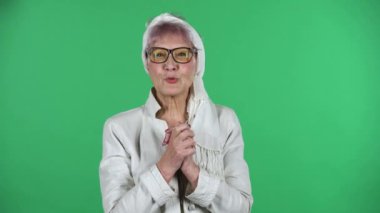Yaşlı stil sahibi kadının portresi kameraya heyecanla bakıyor, sonra da yeşil arka planda izole edilmiş zaferini kutluyor..