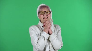 Yaşlı stil sahibi kadının portresi, yeşil arka planda soyutlanmış kollarıyla şefkatle bakıyor..