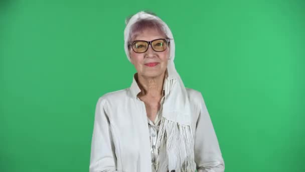 Porträt der alten stilvollen Frau sieht gerade aus und lächelt isoliert über grünem Hintergrund. — Stockvideo
