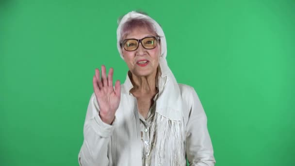 Портрет старой стильной женщины машет рукой и показывает жест приходят сюда изолированы на зеленом фоне. — стоковое видео