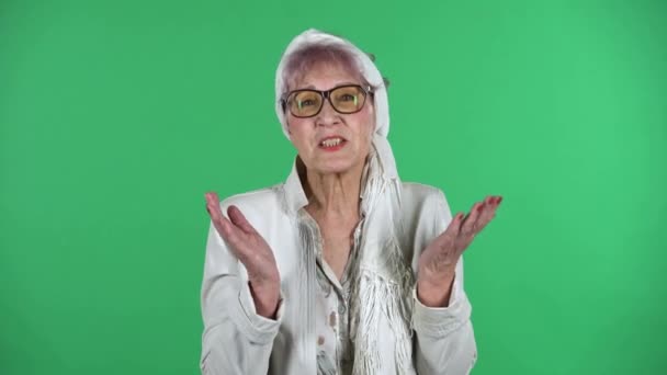 Portrait of old stylish woman is communicates with someone frustrated isolated over green background. — Stock Video