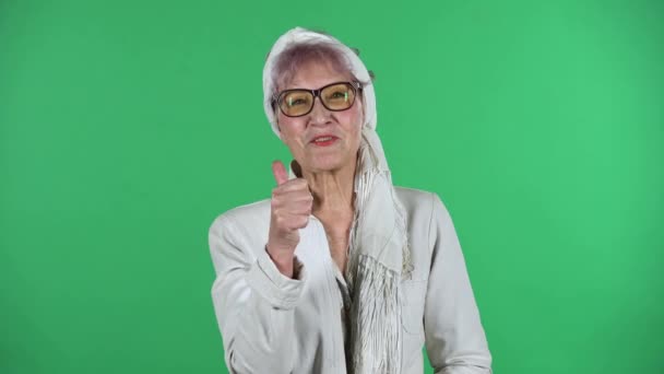 Portrait of old stylish woman is showing thumbs up, gesture like, isolated over green background. — Stock Video