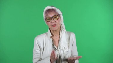 Yaşlı bir kadının portresi üzgün, yeşil arka planda izole edilmiş bir şekilde ellerini sallıyor..