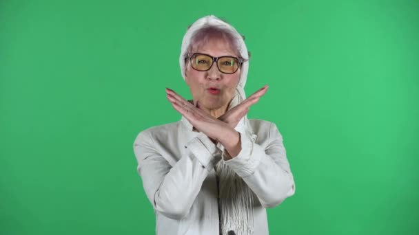 Retrato de velha mulher elegante é estritamente gestual com as mãos cruzadas fazendo X forma significado negação dizendo NÃO isolado sobre fundo verde. — Vídeo de Stock