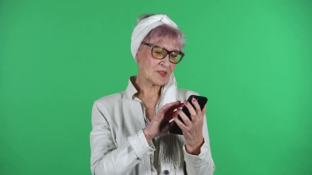 Portrait of old stylish woman is texting on her phone isolated over green background. — Stock Video