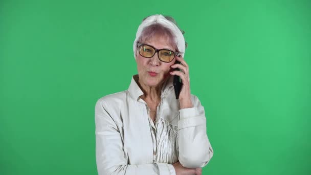 Retrato de la vieja mujer con estilo está hablando para el teléfono móvil aislado sobre fondo verde. — Vídeos de Stock