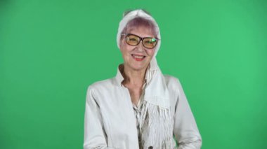 Yaşlı, şık bir kadının portresi, yeşil arka planda saklanmış bir şekilde dümdüz ve gülümsüyor..