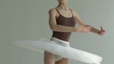 Balarina 'nın gövdesi bir ışık stüdyosunda beyaz bir arka planda piruet hareketi yapıyor. Beyaz bale eteği dansta dönüyor. Kapatın. Yavaş çekim.