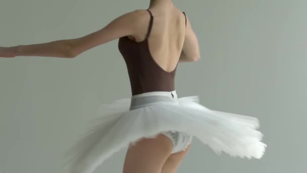 Trup balaríny provádějící pohyb piruety na bílém pozadí v lehkém studiu. Bílá baletní sukně se točí v tanci. Zavřít. Zpomalený pohyb. — Stock video