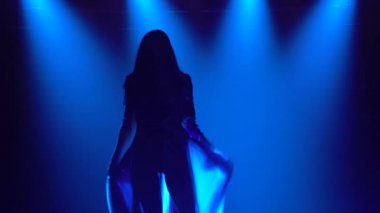 Karanlık bir stüdyoda duman ve mavi neon ışıklarla dans eden bir kızın silueti. Çekici esmer, seksi takım elbiseli, İngiliz bayrağı ve yapay elmasları renginde. Çağdaş kadın dans gösterisi.