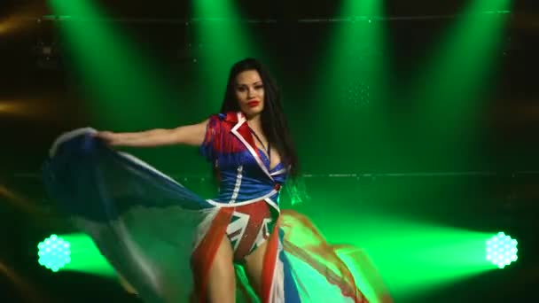 Chica apasionada bailando en un traje sexy en el color de la bandera inglesa y diamantes de imitación. Atractiva morena en un estudio oscuro con humo y luces de neón verde. Sexy espectáculo de danza femenina. — Vídeos de Stock