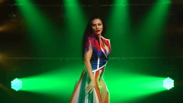 Gepassioneerd meisje dansend in een sexy pak in de kleur van de Engelse vlag en steentjes. Aantrekkelijke brunette in een donkere studio met rook en groene neon lichten. Sexy vrouw dans show. — Stockvideo