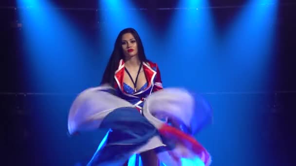 Mulher apaixonada dançando em um terno sexy na cor da bandeira inglesa e strass. Morena atraente acenando sua saia em um estúdio escuro com fumaça e luzes de néon azul. Show de dança feminina. — Vídeo de Stock