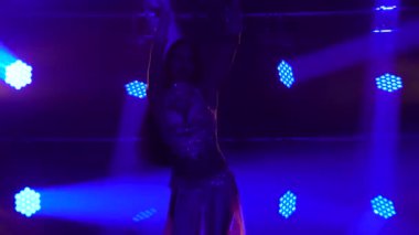 Dans ederken vücudun esnekliğini ve cinselliğini gösteren büyüleyici bir doğulu dansçı. Sosyetik doğulu kostümlü, esmer bir kız. Duman ve mavi neon ışıklarla karanlık stüdyoda çekildi. Siluet.