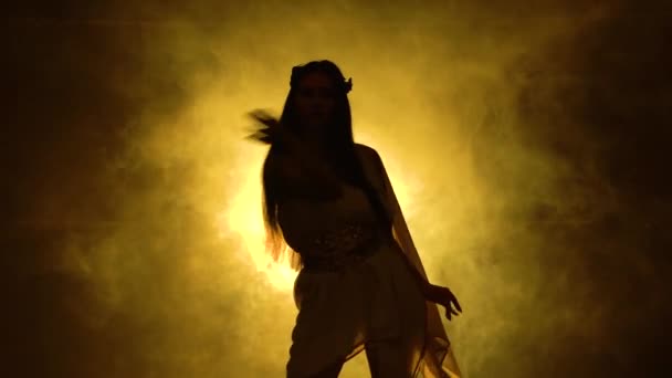 Burning brunette is dancing in a nightclub in the dark and dynamic neon lights. Smoky background. Dancing go go. Silhouette girl in greek greece goddes dress and wreath high fashion. — Stock Video