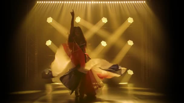 Chica joven bailando en un estudio oscuro con humo y luces de neón amarillo. Silhouette atractiva morena en un traje sexy en el color de la bandera británica y diamantes de imitación. Espectáculo de danza femenina contemporánea. — Vídeos de Stock