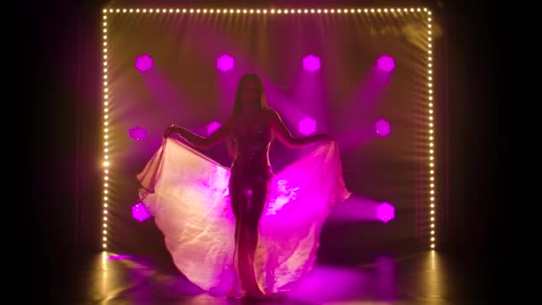 Bailarina oriental es un baile apasionado sobre un fondo púrpura en el humo. Silueta esbelta chica alta en un traje oriental tachonado de diamantes de imitación. — Vídeo de stock