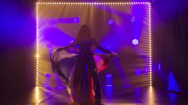 Silhueta fina alta mulher dançando em um terno sexy na cor da bandeira inglesa e strass. Morena atraente acenando sua saia em um estúdio escuro com fumaça e luzes de néon azul. Devagar. — Vídeo de Stock