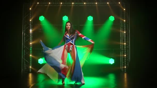 Chic kvinna dansar i en sexig kostym i färgen på den engelska flaggan och strass. Attraktiv brunett i en mörk ateljé med rök och grönt neonljus. Sexig kvinnlig dansshow. Långsamma rörelser. — Stockvideo