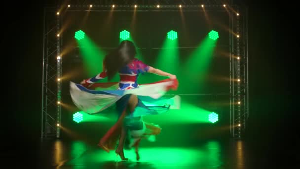 Femme chic dansant dans un costume sexy dans la couleur du drapeau anglais et des strass. Jolie brune dans un studio sombre avec de la fumée et des néons verts. Spectacle de danse féminine sexy. Mouvement lent. — Video