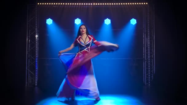 Schlanke, hohe Frau, die in einem sexy Anzug in der Farbe der englischen Flagge und Strass tanzt. Attraktive Brünette schwenkt ihren Rock in einem dunklen Studio mit Rauch und blauem Neonlicht. Zeitlupe. — Stockvideo