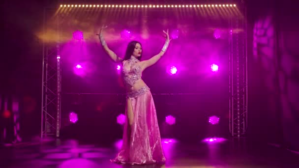 Красивая восточная танцовщица живота танцует и демонстрирует гибкость и привлекательность своего тела. Фиолетовый фон в дыму. Медленное движение. — стоковое видео