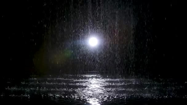 暗いスタジオでのスポットライトを背景に雨が降ります。スローモーション. — ストック動画