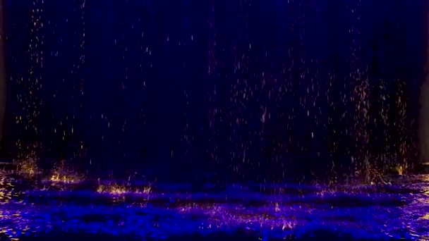 Modré cákance dopadají na vodní hladinu, která září. Černé pozadí. Neonové osvětlení v temném studiu. Zpomalený pohyb. — Stock video