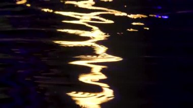 Suyun dalgalanan yüzeyinde parlak bir ışık çizgisi. Siyah arka plan. Kapatın. Yavaş çekim.