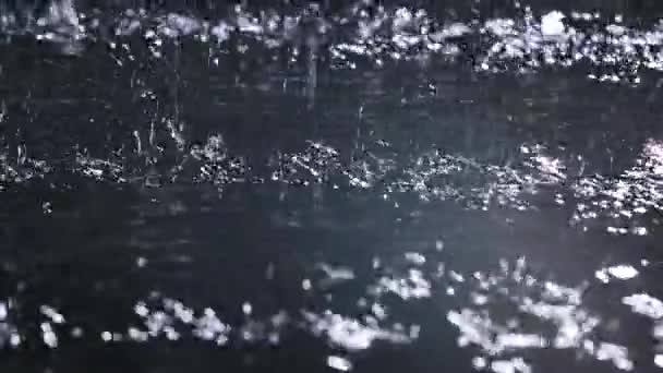 Блестящие капли дождя падают на поверхность воды на черном фоне. Медленное движение. Закрыть. — стоковое видео