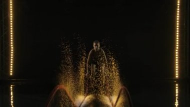 Savaş halatları seansı. Çekici genç, formda bir sporcu. Spor salonunda çalışıyor. Savaş halatlarıyla egzersiz yapıyor. Siyah arka plan. Yavaş çekim.