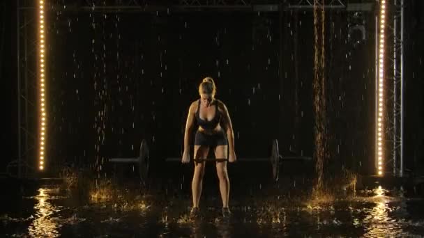 Приваблива молода спортсменка піднімає бар над головою. Дощі падають на м'язове тонке тіло жінки. Чорний фон і неонові прожектори в студії. Повільний рух . — стокове відео