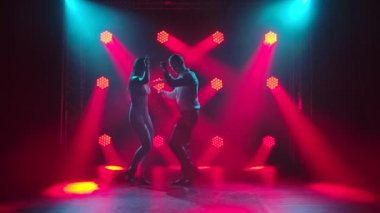 Dans eden genç çift Latin müziği. Bachata, merengue, salsa. Arka planda neon ışıkları olan karanlık bir stüdyoda çekilmiş..