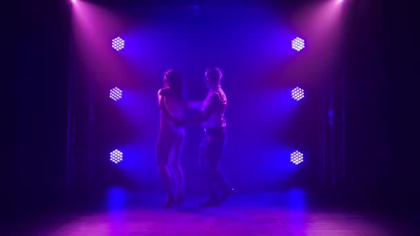 Молодая пара танцует латинскую музыку. Бачата, меренге, сальса. Снято в темной студии с неоновыми огнями на заднем плане. — стоковое видео