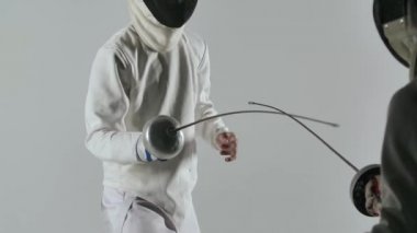 Stüdyoda beyaz arka planda iki eskrimci düellosu. İki profesyonel eskrimci, folyo savaşlarında usta bir kılıç ustası. Ağır çekim. Kapat..