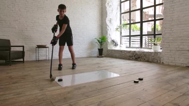 Um menino jogador de hóquei treina com um bastão de hóquei e disco em uma superfície escorregadia dentro de casa. Movimento lento. — Vídeo de Stock