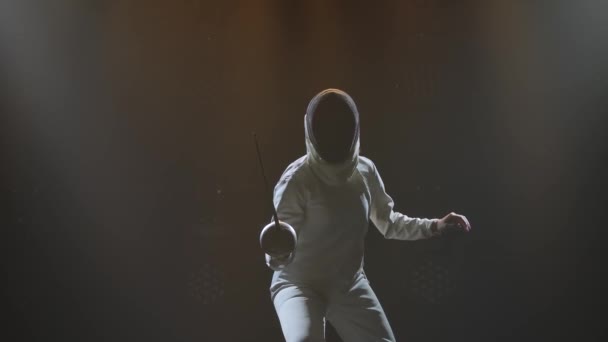 Fencer žena trénuje šerm cvičení ve studiu uvnitř. Sportovkyně cvičí útok na protivníka. Černé zakouřené pozadí. Zpomal. Zavřít. — Stock video