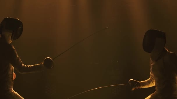 Вид збоку два професійні фехтувальники демонструють майстерну боротьбу з мечами у своїй фользі. Постріл ізольований на чорному тлі з м'яким жовтим світлом. Повільний рух. крупним планом . — стокове відео