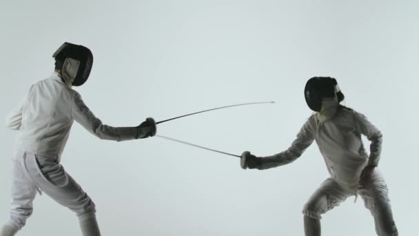 Deux escrimeurs professionnels font preuve de maîtrise dans leur combat à l'épée. Ils esquivent, sautent, sautent et sautent. Tourné isolé sur fond blanc. Au ralenti. Gros plan. — Video