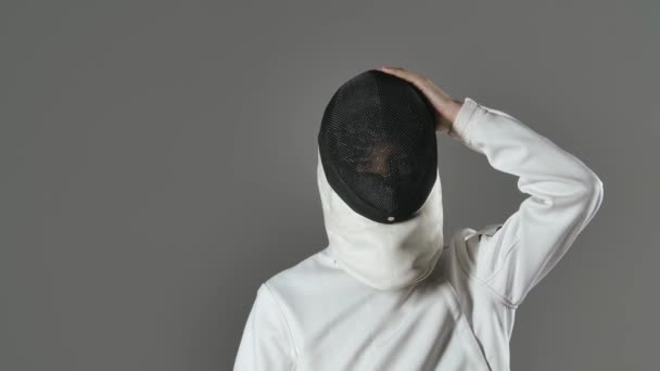 Отслеживание замедленной съемки профессионального фехтовальщика в белом защитном костюме, носящего защитную маску и держащего в руке защитную фольгу. Изолированный серый фон. Закрыть. — стоковое видео