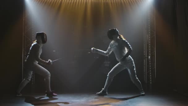 Side view duel of two women fencers. Sportswomen practice strikes, attack and defend. Filmed indoors with studio light. Slow motion. — Stock Video