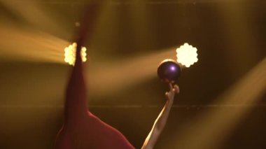 Sporcu kız jimnastikçi kız topla akrobatik egzersizler yapıyor ve esneme hareketleri yapıyor, vücudunun esnekliğini gösteriyor. Neon ışıkları olan karanlık bir stüdyoda çekilmiş. Kapat..