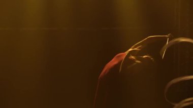 Aktif bir genç kız ipek kurdeleyle jimnastik yapıyor ve ileri geri taklalar atıyor. Stüdyoda, üzerinde duman ve sarı yumuşak ışık olan bir kadının silueti. Kapat..