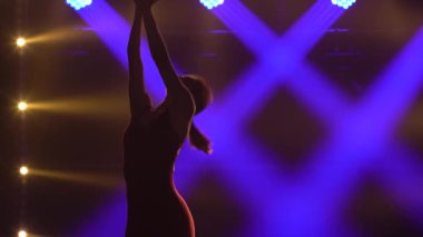 Mor spot ışıklarının altında, genç bir jimnastikçi bir topla akrobatik egzersizler yapıyor. Sıska, çekici bir kızın silüeti. Dar bir spor ceket içinde. Kapat..