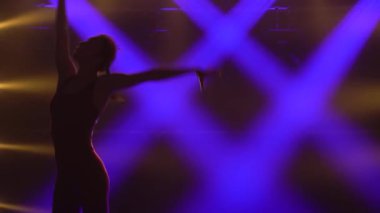 Mor spot ışıklarının altında, genç bir jimnastikçi bir topla akrobatik egzersizler yapıyor. Sıska, çekici bir kızın silüeti. Dar bir spor ceket içinde. Kapat..