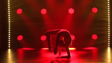 Esmer genç kadınlar ritmik jimnastik dansı yapıyor. Kırmızı spot ışıklarının arka planında siluetler. Kapat..